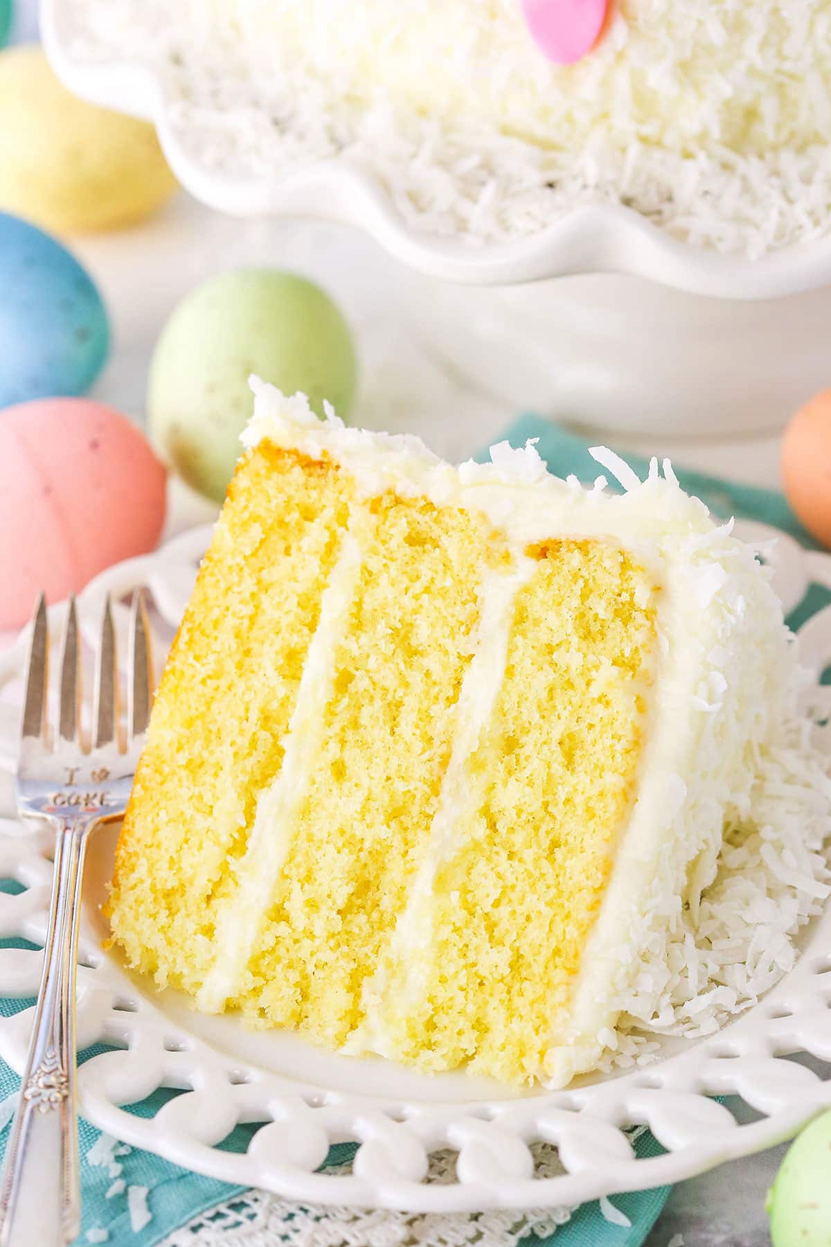Overhead view of a slice of Easter Bunny Cake on a white plate with a fork with painted Easter eggs surrounding