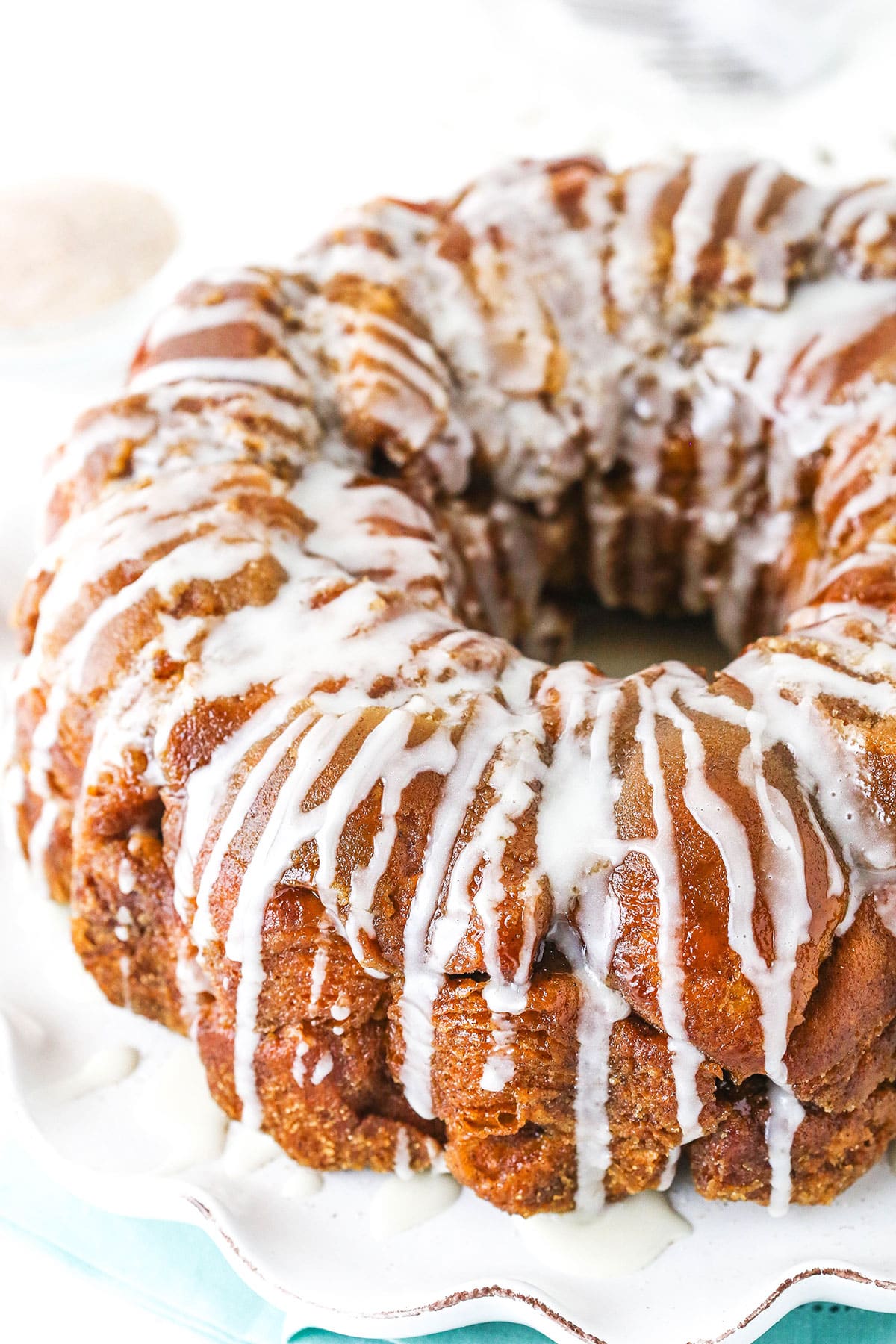 This EASY Monkey Bread recipe is made with balls of refrigerated biscuit dough rolled in cinnamon-sugar and coated with brown sugar sauce. Stick them all in a pan, bake and drizzle with a quick vanilla icing. Totally irresistible! Top view of homemade monkey bread on a white plate
