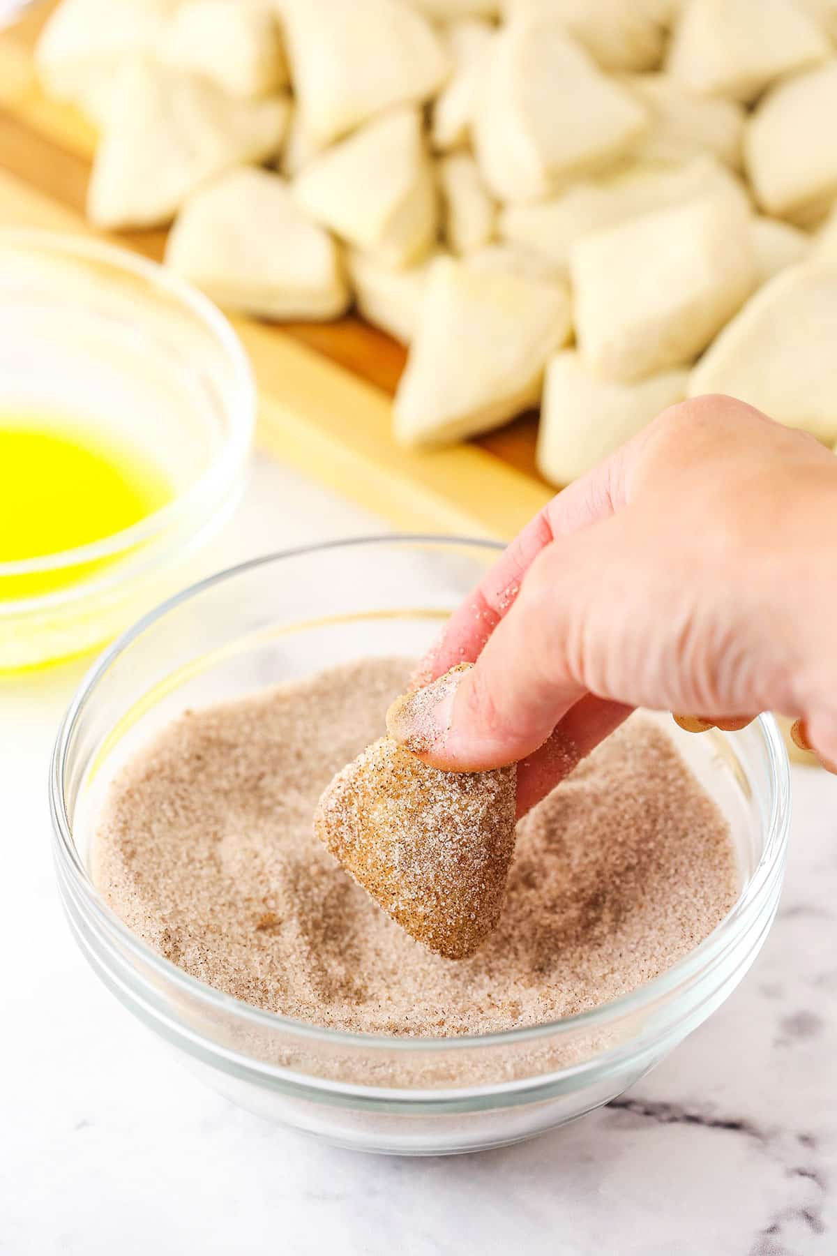 Making Monkey Bread Step showing the biscuit coated in butter being dipped into cinnamon sugar