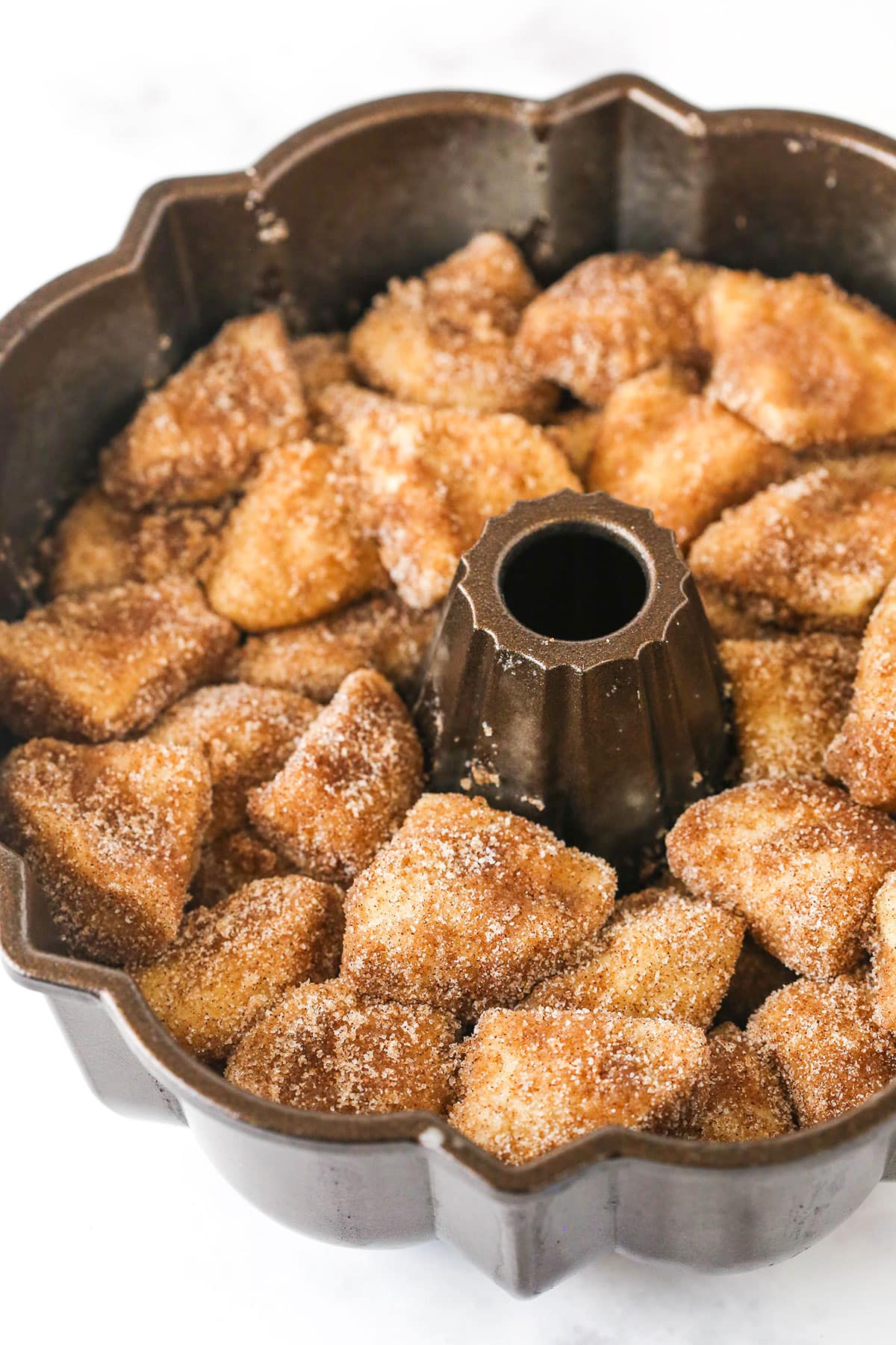 Making Monkey Bread Step showing all the biscuit pieces coated in cinnamon sugar being layered into the pan