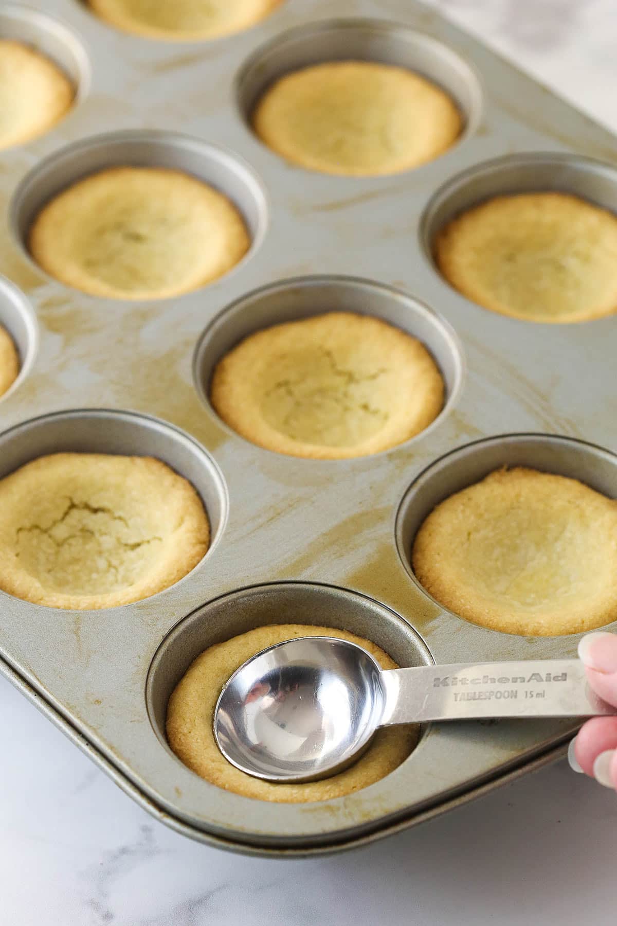 Using a tablespoon to make a divot in sugar cookies baked in cupcake tins.
