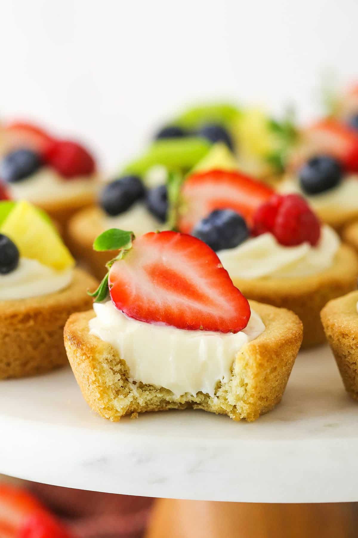 An easy fruit cheesecake sugar cookie cup with a bite taken out of it.