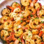 Close view of Garlic Butter Shrimp Scampi in a metal pan with cut lemons in the background