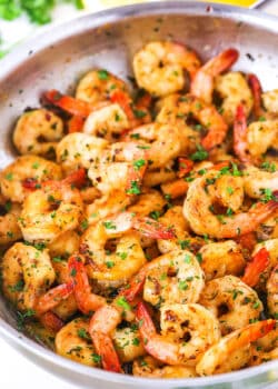 Close view of Garlic Butter Shrimp Scampi in a metal pan with cut lemons in the background