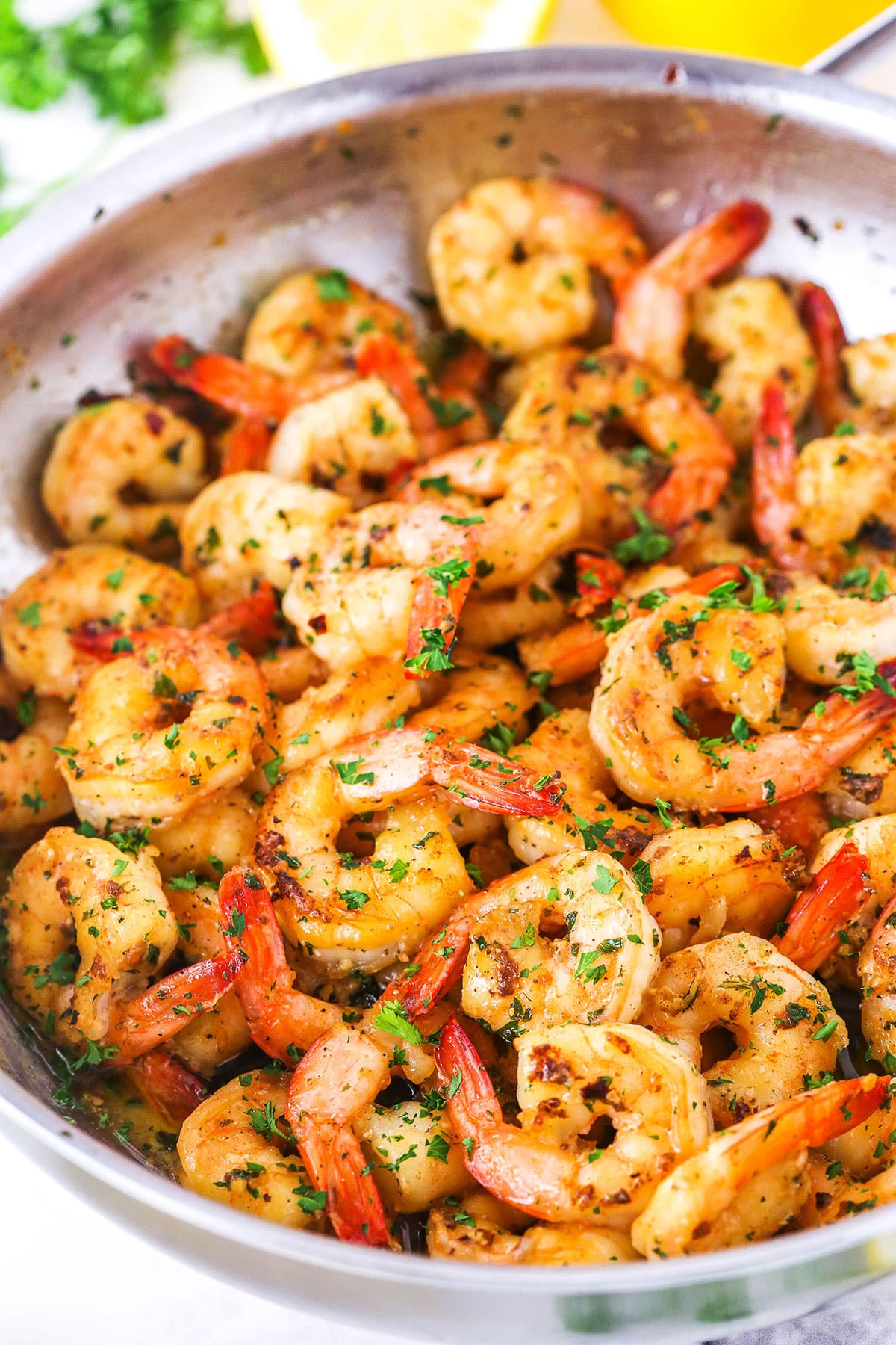 Close view of Garlic Butter Shrimp Scampi in a metal pan with cut lemons in the background