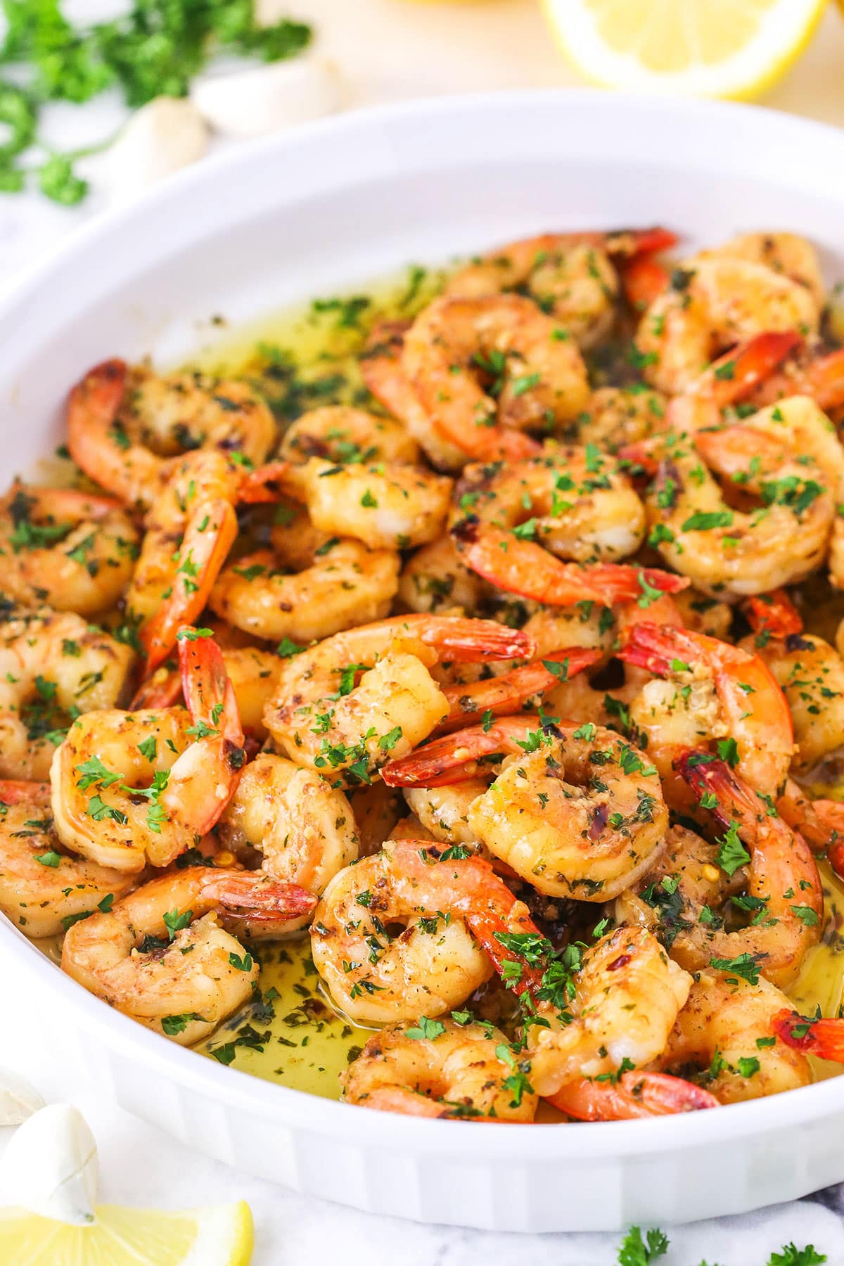 Side view of Garlic Butter Shrimp Scampi in a white platter with cut lemons in the background