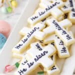 "He Is Risen" Cutout Cookies stacked on a white platter with decorative pink roses