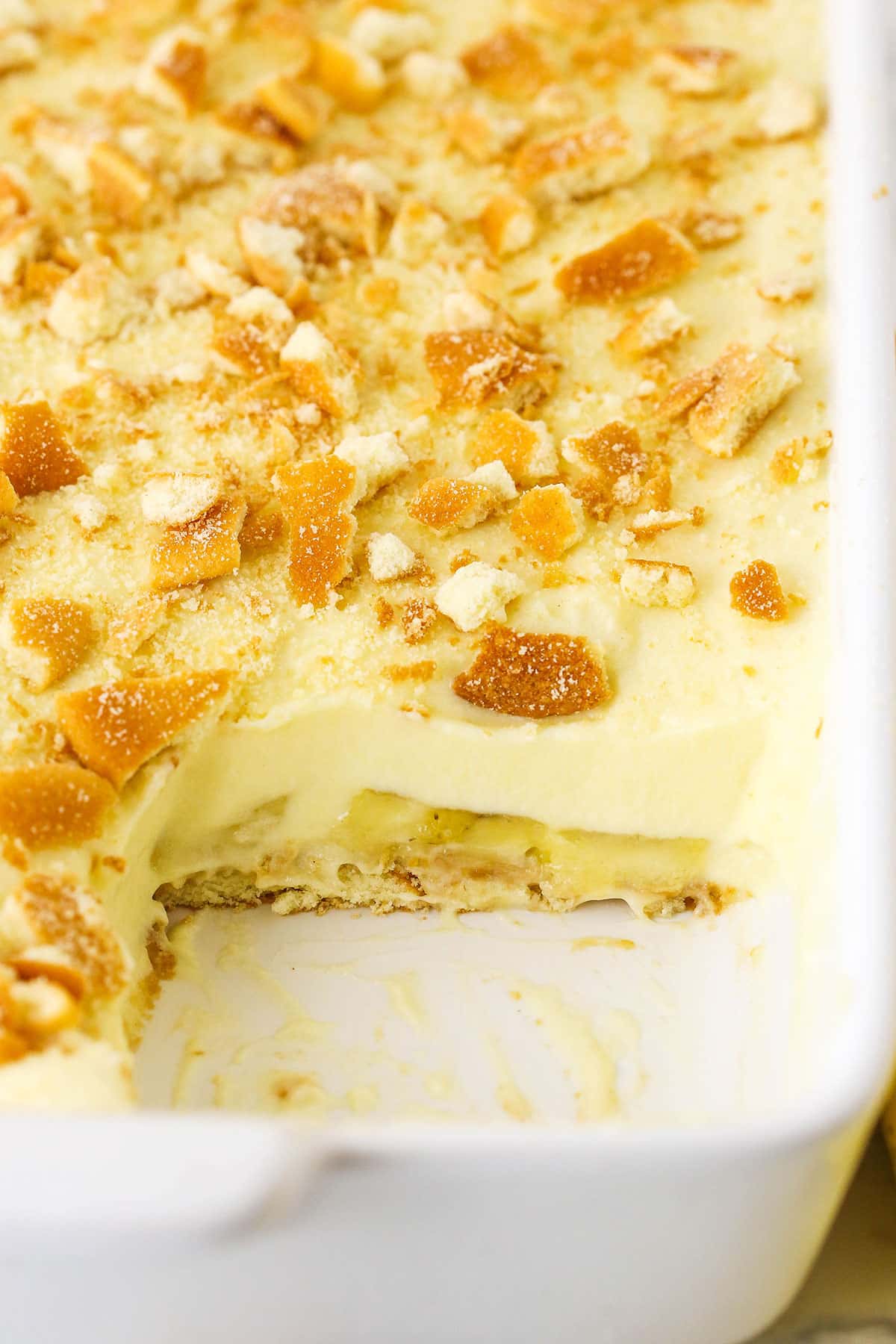 Homemade Banana Pudding topped with crushed vanilla wafers in a white platter with one serving removed