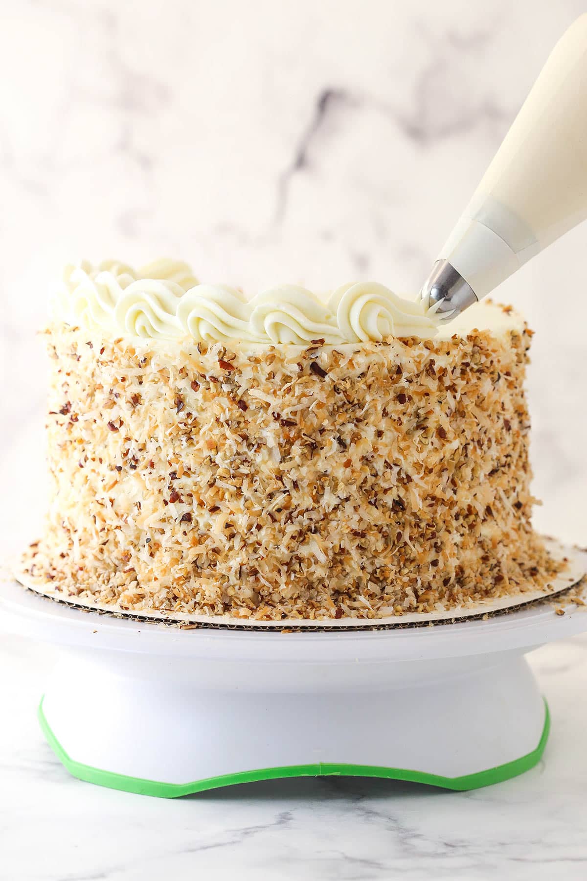 Piping frosting around the edges of Italian cream cake.