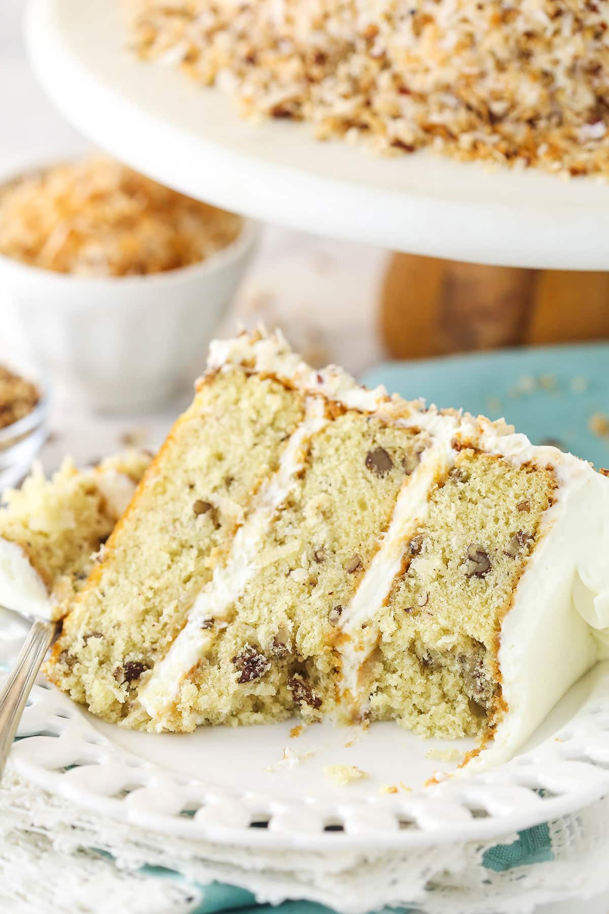 A slice of Italian cream cake on a plate with a bite taken out of it.