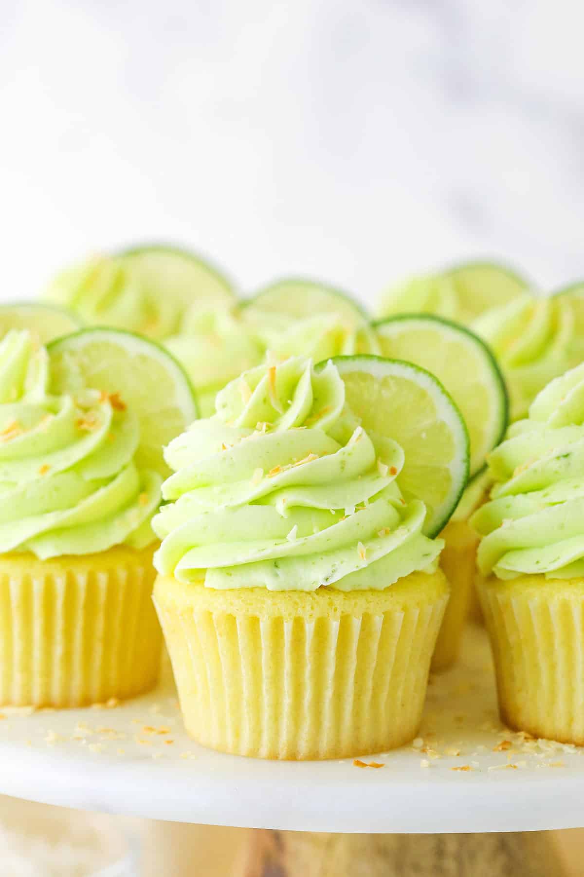 Side view of Key Lime Coconut Cupcakes on a cake stand