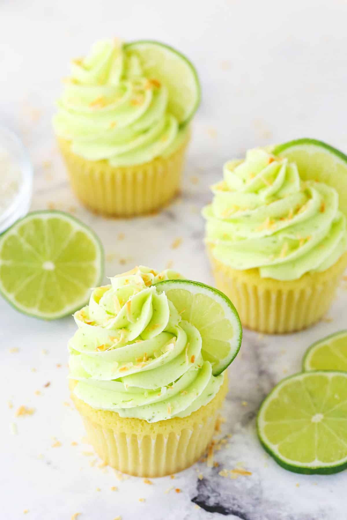 These key lime coconut cupcakes are made of soft, fluffy coconut cupcakes topped with zesty key lime buttercream. They're a tropical dream! Overhead image of three key lime coconut cupcakes.
