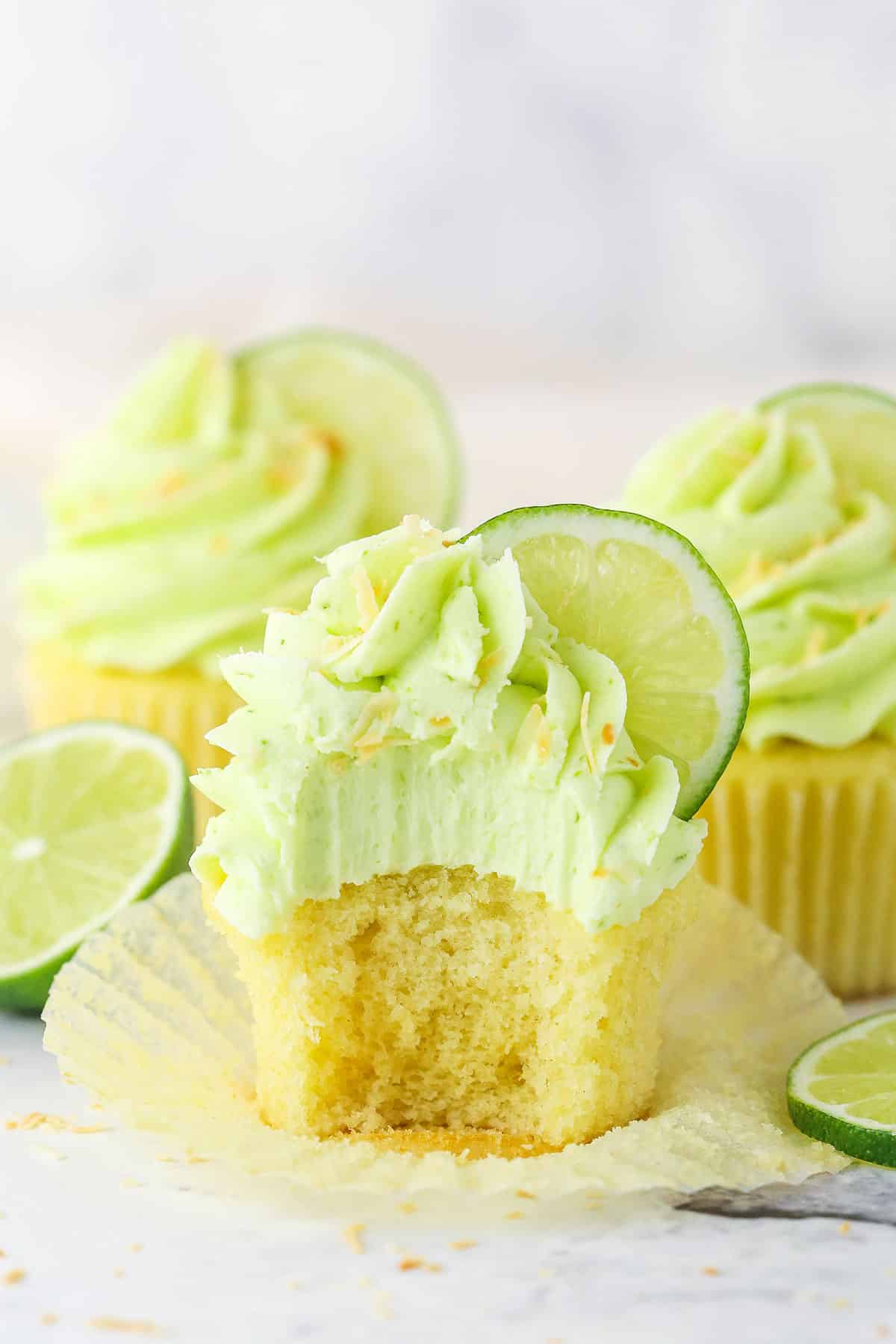 These Key Lime Coconut Cupcakes are a delectable treat for summer! Moist coconut cupcakes are topped with key lime buttercream frosting! Side view of a Key Lime Coconut Cupcake with a bite taken out