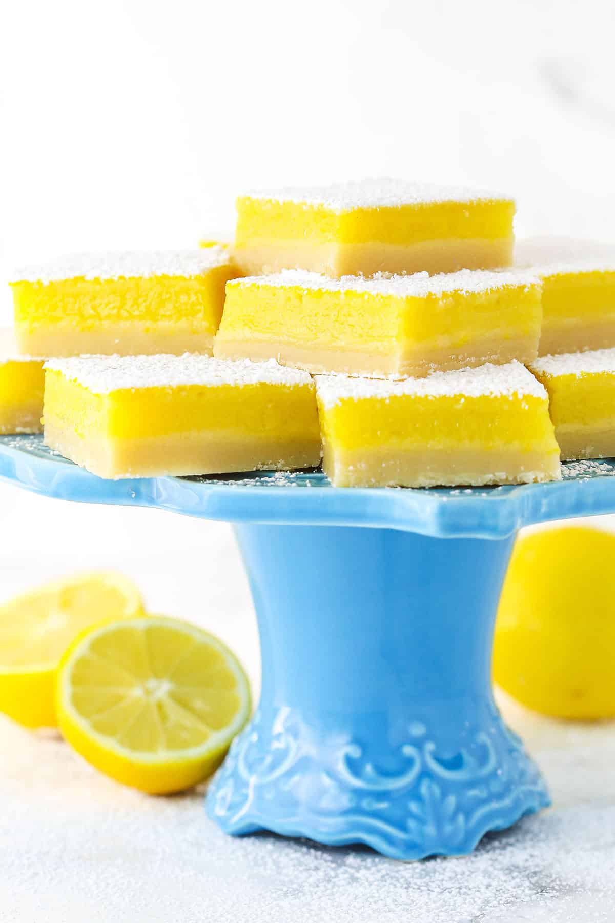 Lemon bars on a blue cake stand surrounded by lemons