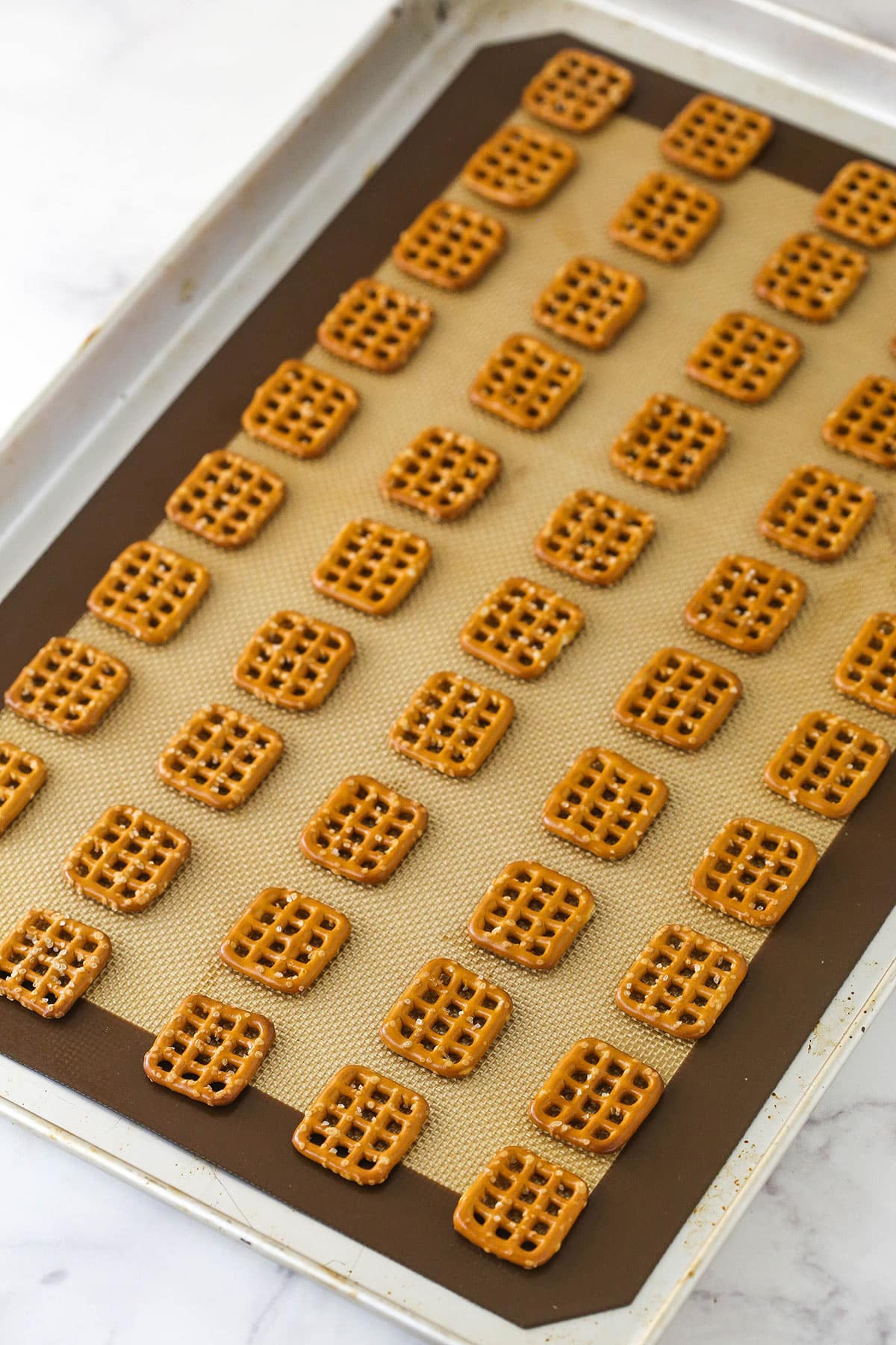 lots of square pretzels laid out on silicone baking mat on baking sheet