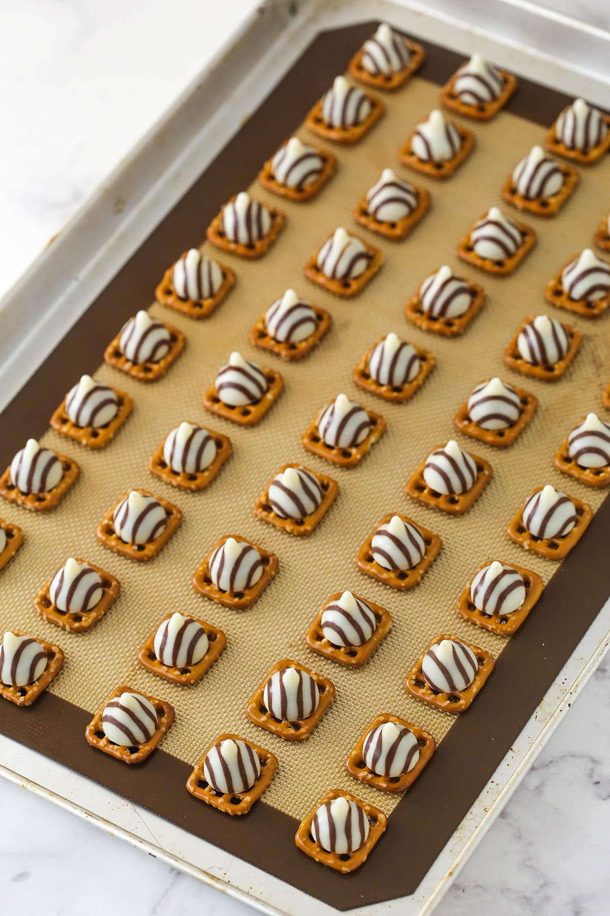 lots of square pretzels laid out on silicone baking mat on baking sheet with hugs on top of each