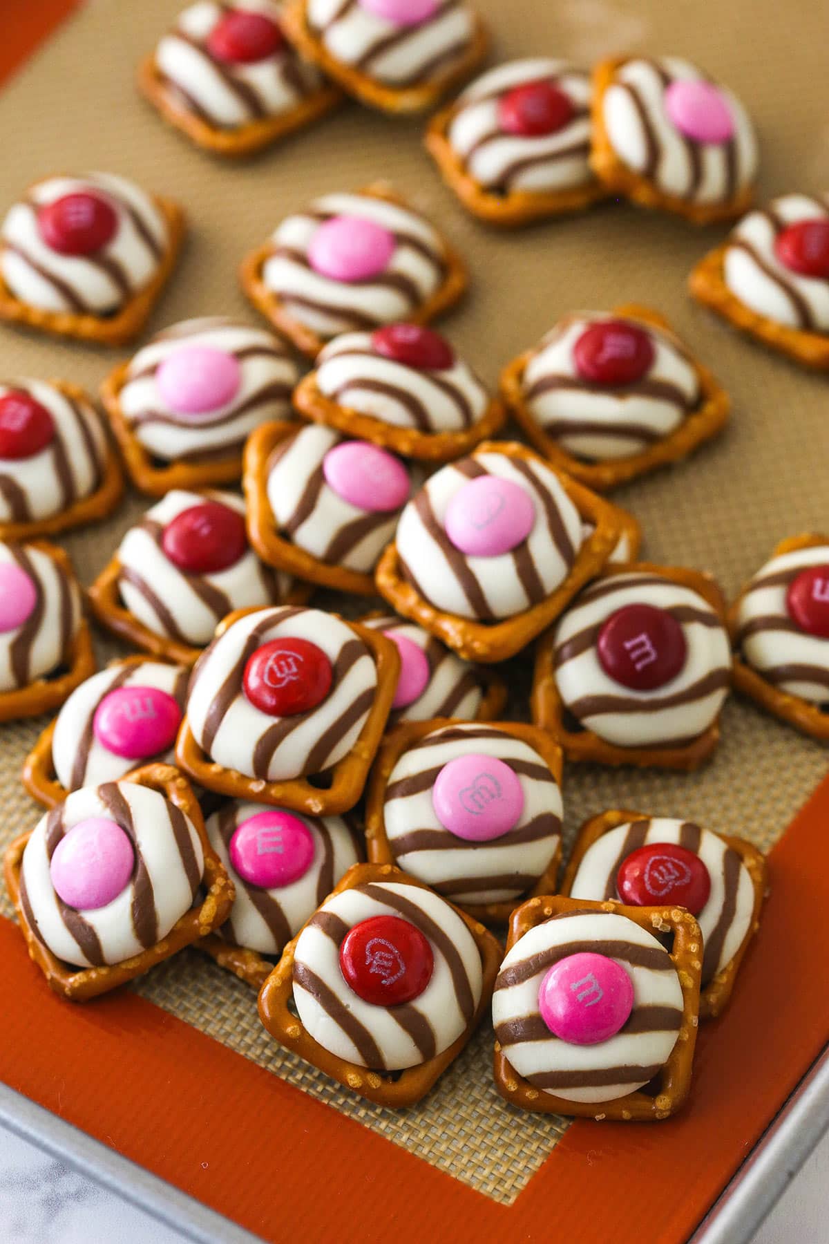 pink and red valentine's day pretzel M&M hugs in a pile on a silicone mat on a cookie sheet