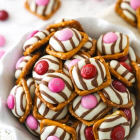 Assorted pink and red M&M pretzel hugs in a fluted white bowl.