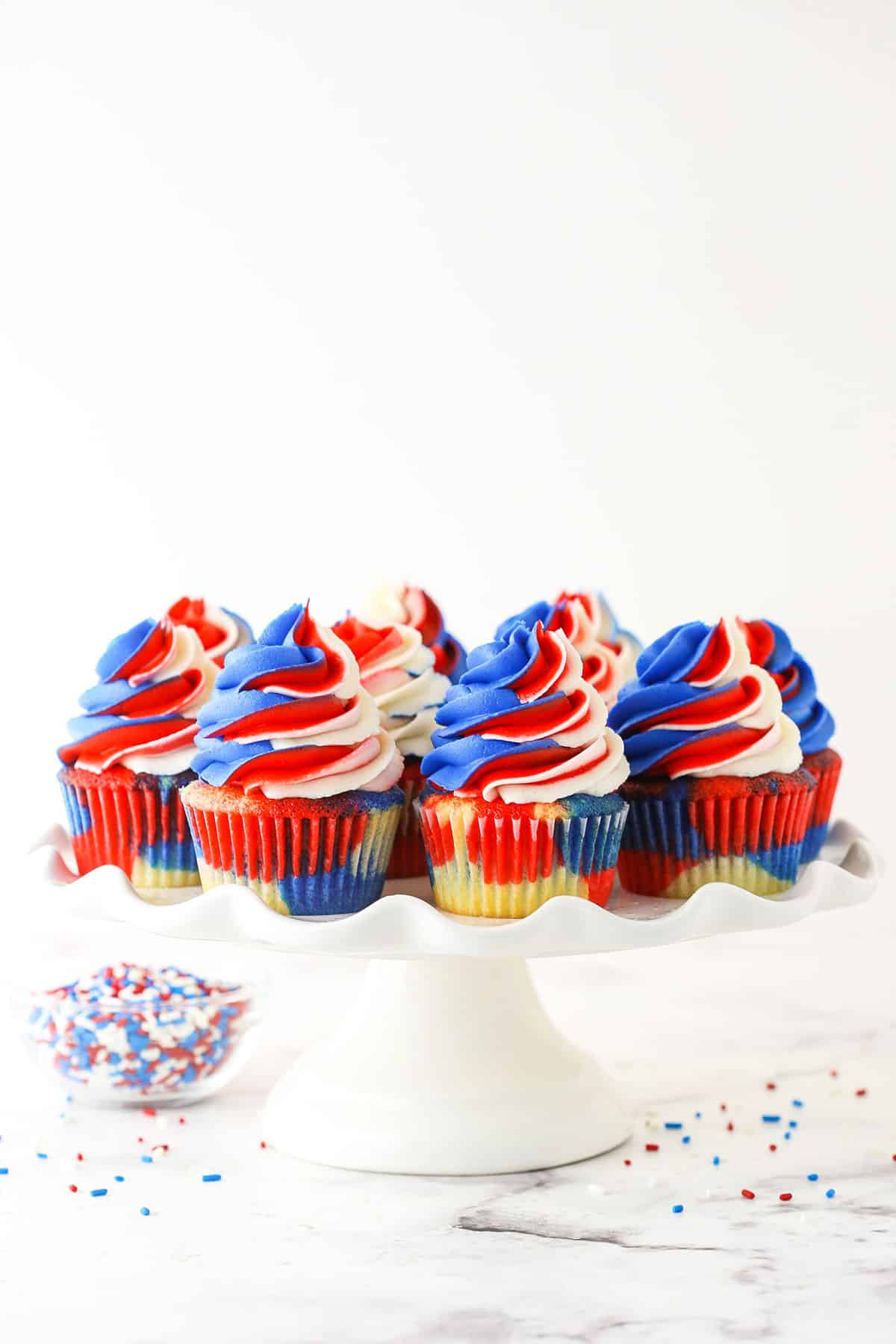 zoomed out photo of cupcakes on a white cake stand