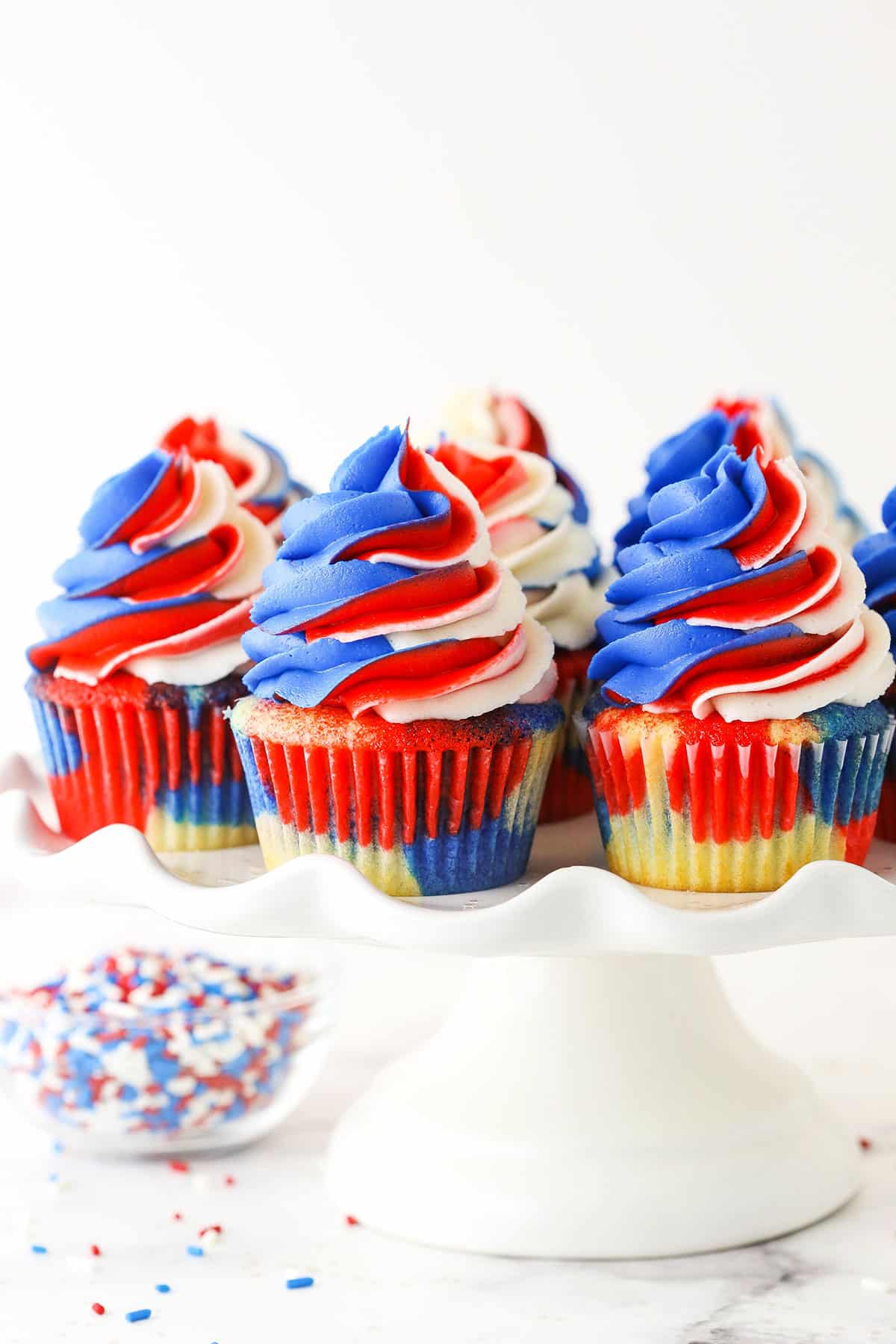 These Red, White and Blue Swirl Cupcakes are so festive and perfect for celebrating July 4th! Forget the box mix and make these beauties from scratch! close up of red, white and blue cupcakes on a cake stand