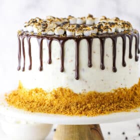 A full S'mores Cake topped with marshmallows and chocolate drip on a cake stand