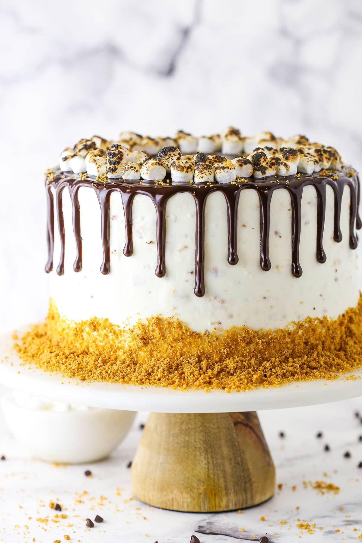 A full S'mores Cake topped with marshmallows and chocolate drip on a cake stand