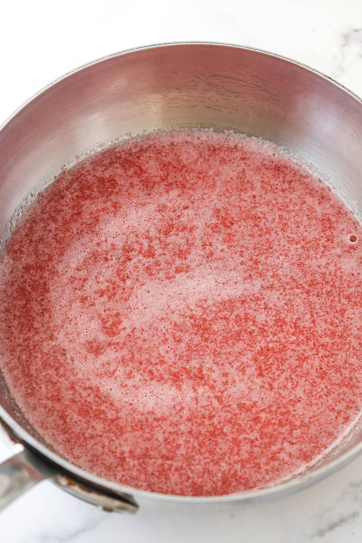 This perfect-for-summer strawberry cheesecake is made of a Graham Cracker crust, a creamy cheesecake filling, and a sweet strawberry sauce. Simmering strawberry sauce in a saucepan.
