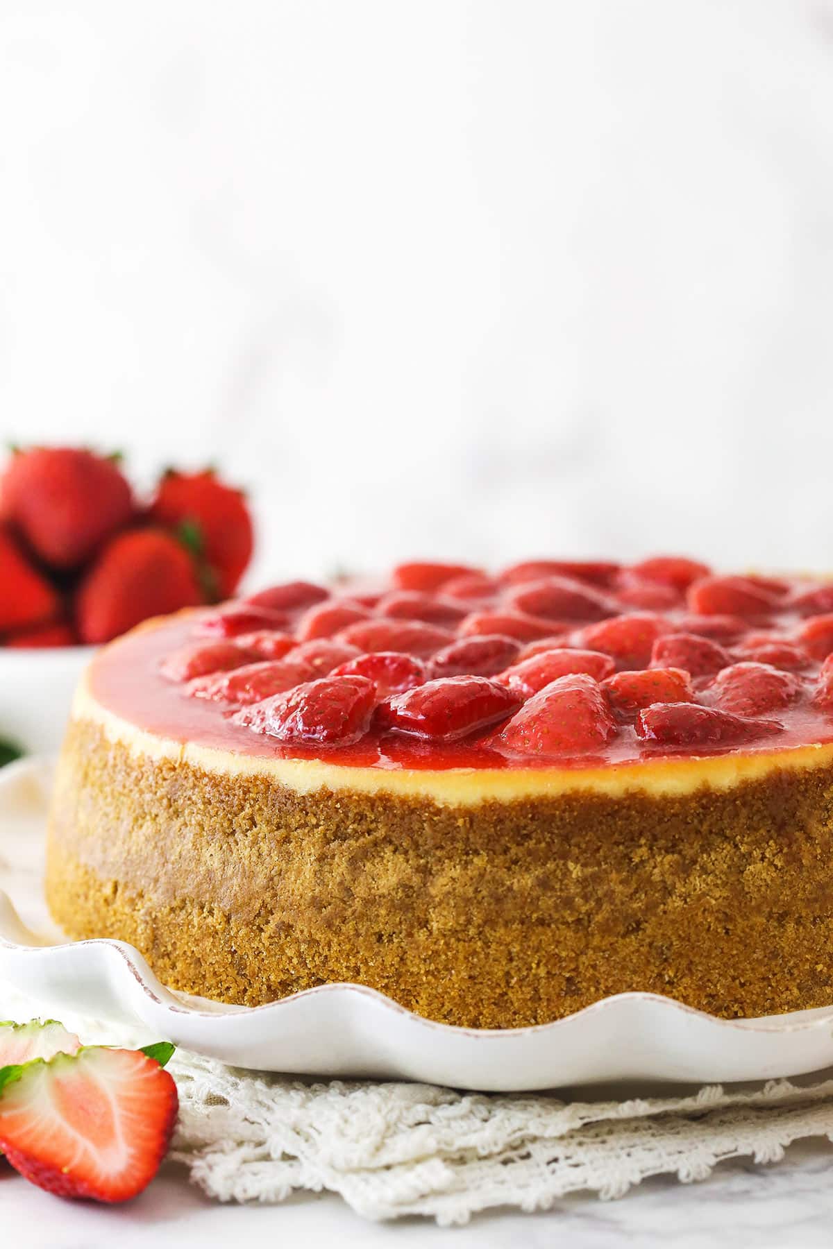 This perfect-for-summer strawberry cheesecake is made of a Graham Cracker crust, a creamy cheesecake filling, and a sweet strawberry sauce. Strawberry cheesecake on a serving platter near a bowl of fresh strawberries.
