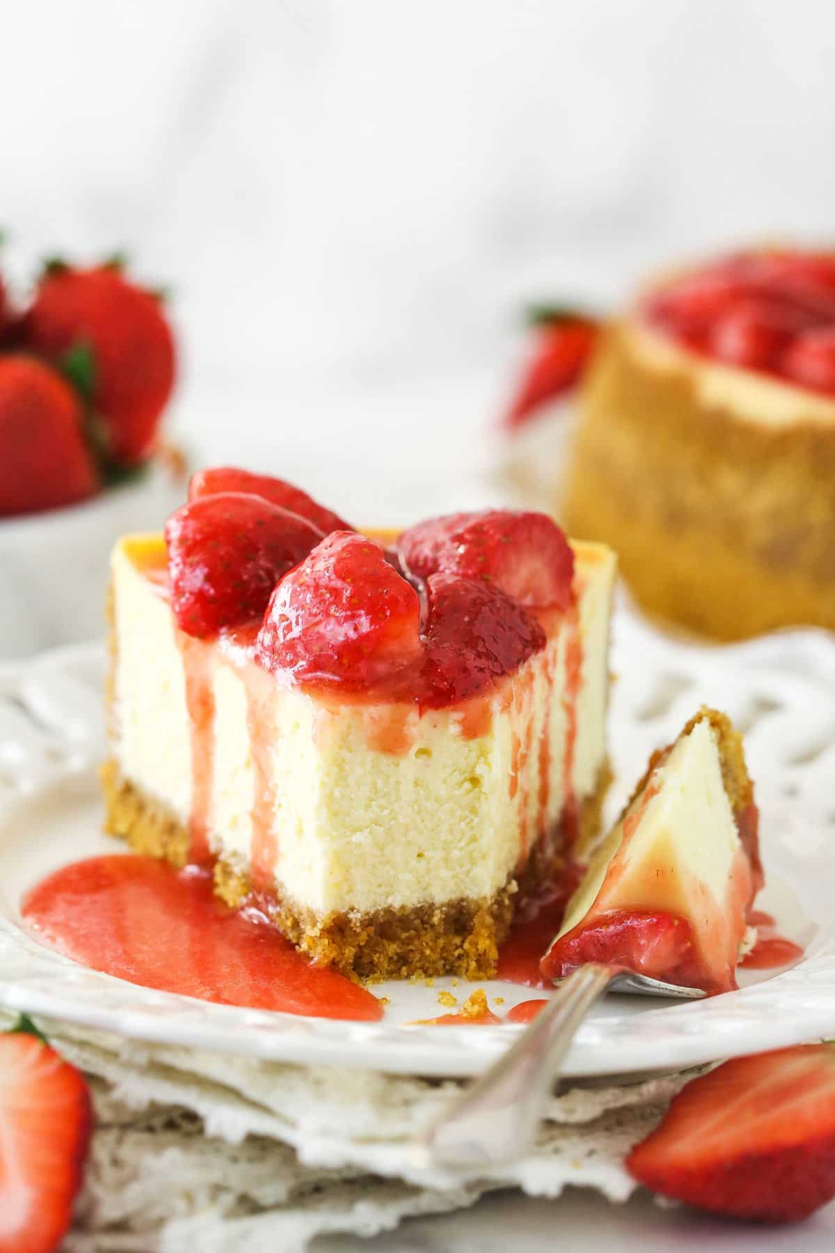 This perfect-for-summer strawberry cheesecake is made of a Graham Cracker crust, a creamy cheesecake filling, and a sweet strawberry sauce. A slice of strawberry cheesecake on a plate with a bite taken out of it.