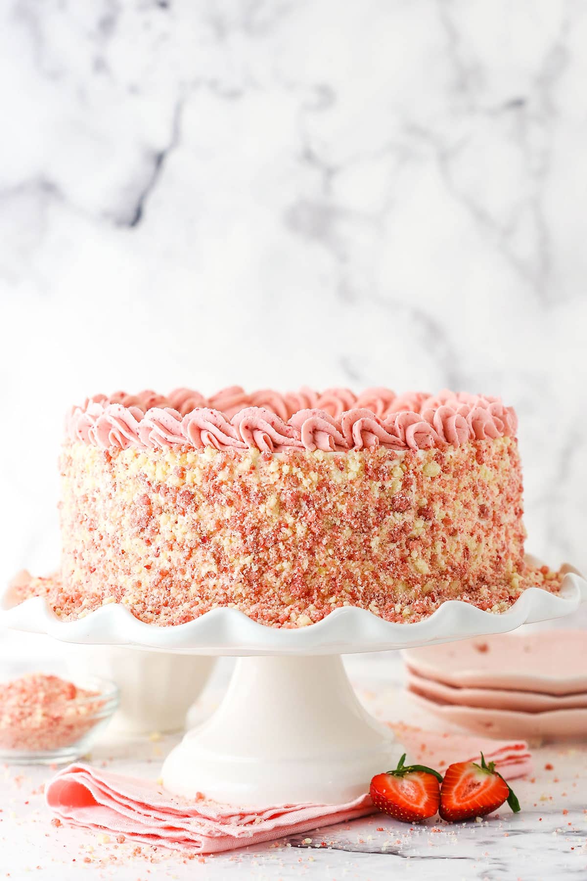 Side view of a full Strawberry Crunchie Ice Cream Cake with pink swirls on a white cake stand