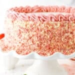 Side view of a full Strawberry Crunchie Ice Cream Cake with pink swirls on a white cake stand