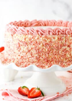 Side view of a full Strawberry Crunchie Ice Cream Cake with pink swirls on a white cake stand