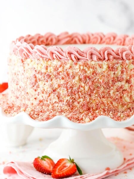 Side view of a full Strawberry Crunchie Ice Cream Cake with pink swirls on a white cake stand