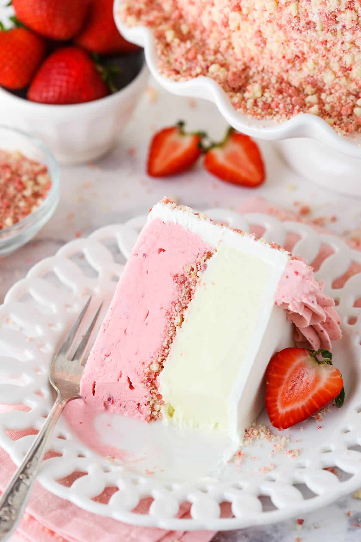 A slice of Strawberry Crunchie Ice Cream Cake with a bite taken out on a white plate with a fork