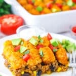 A serving of Taco Tater Tot Casserole topped with chopped avocado and tomato on a white plate with a fork