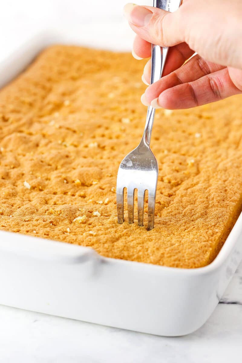 A fork poking holes into the top of the cake for Tres Leches.