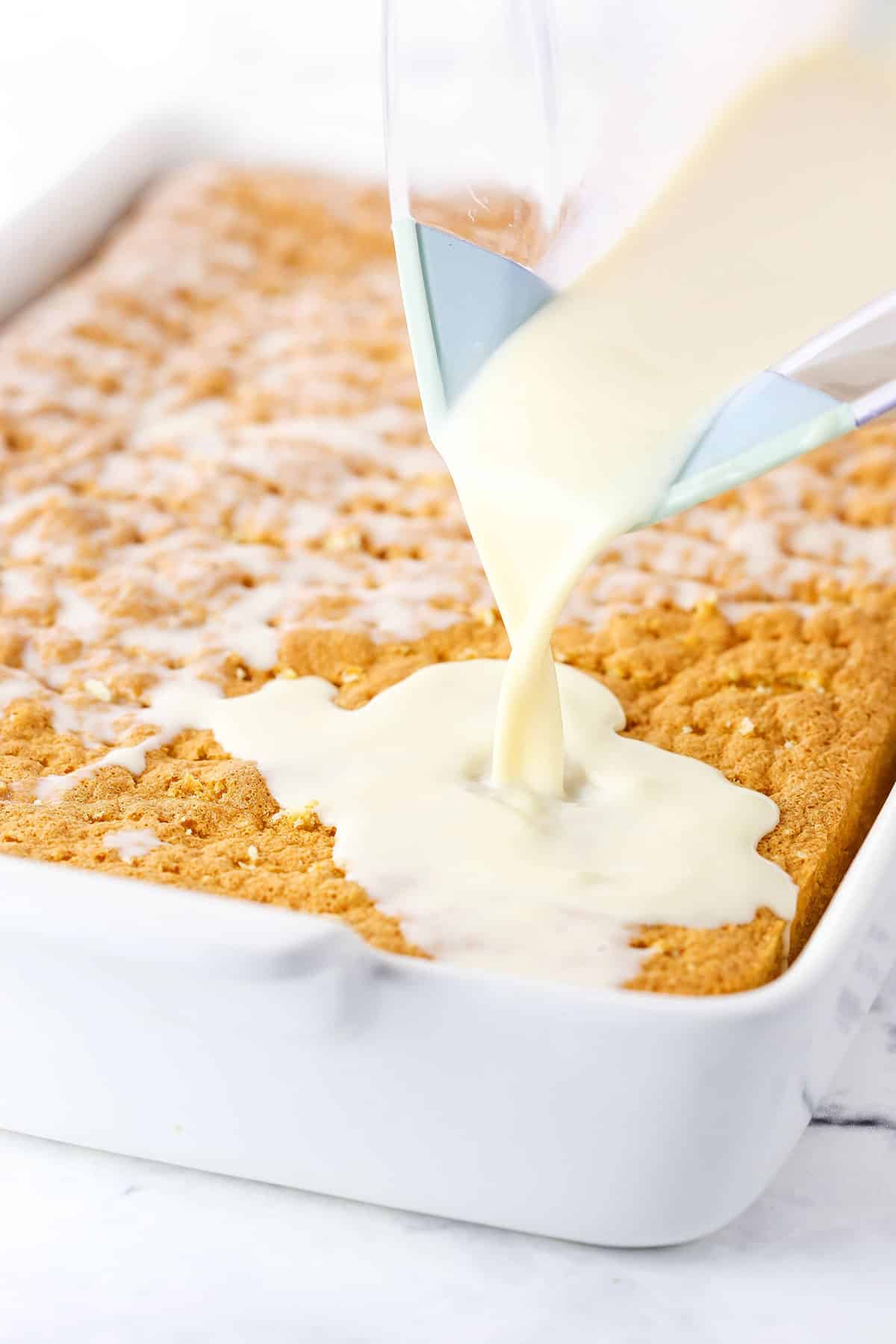 A step in making Tres Leches Cake showing the three milks mixture being poured over the entire cake