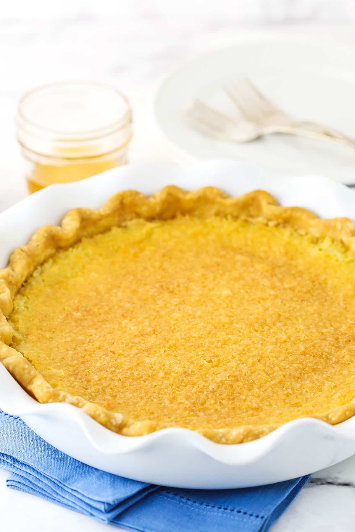 Side view of a full Vinegar Pie in a white platter on a blue place mat