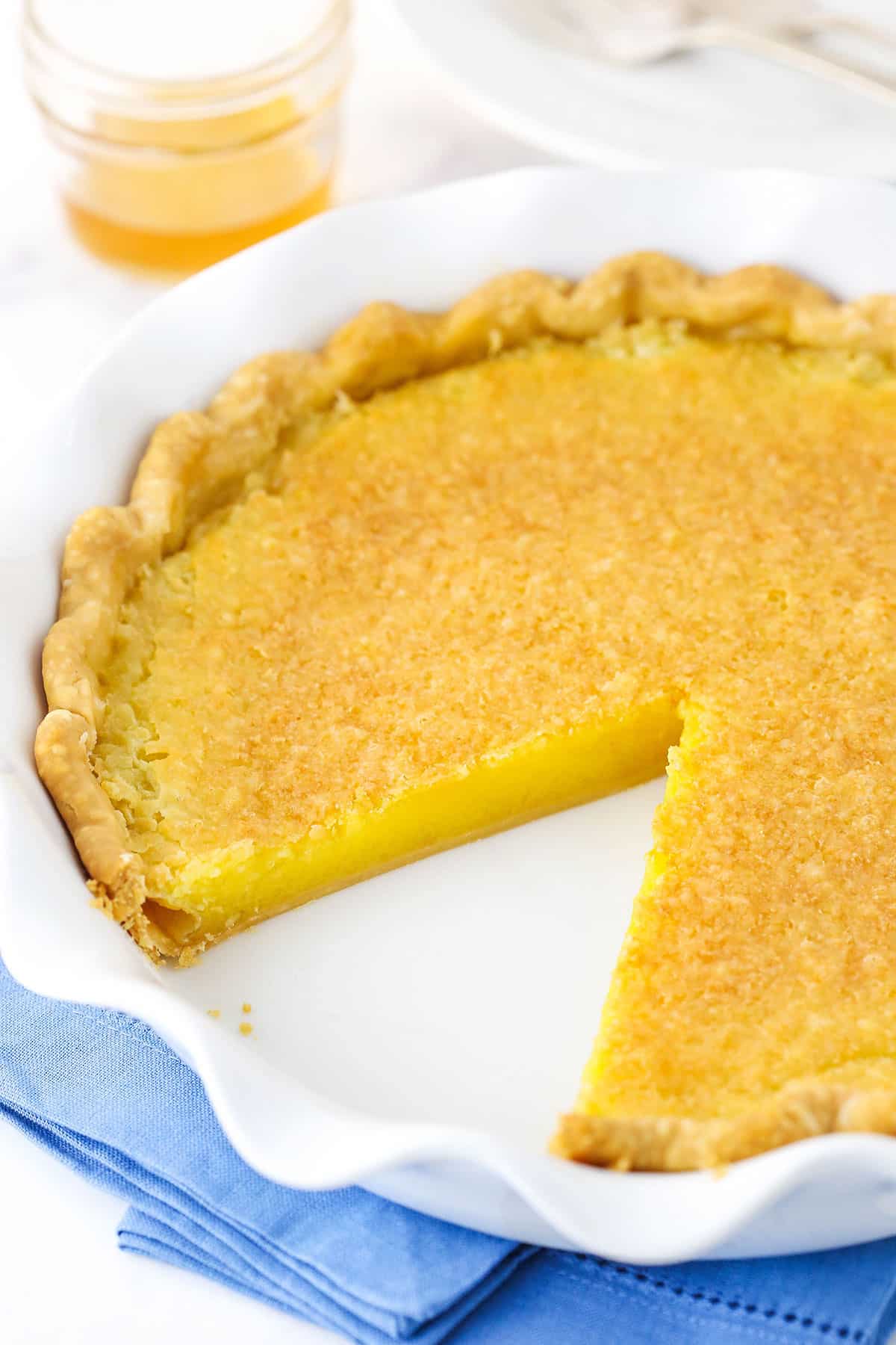 Overhead view of a Vinegar Pie with a slice removed in a white platter on a blue place mat