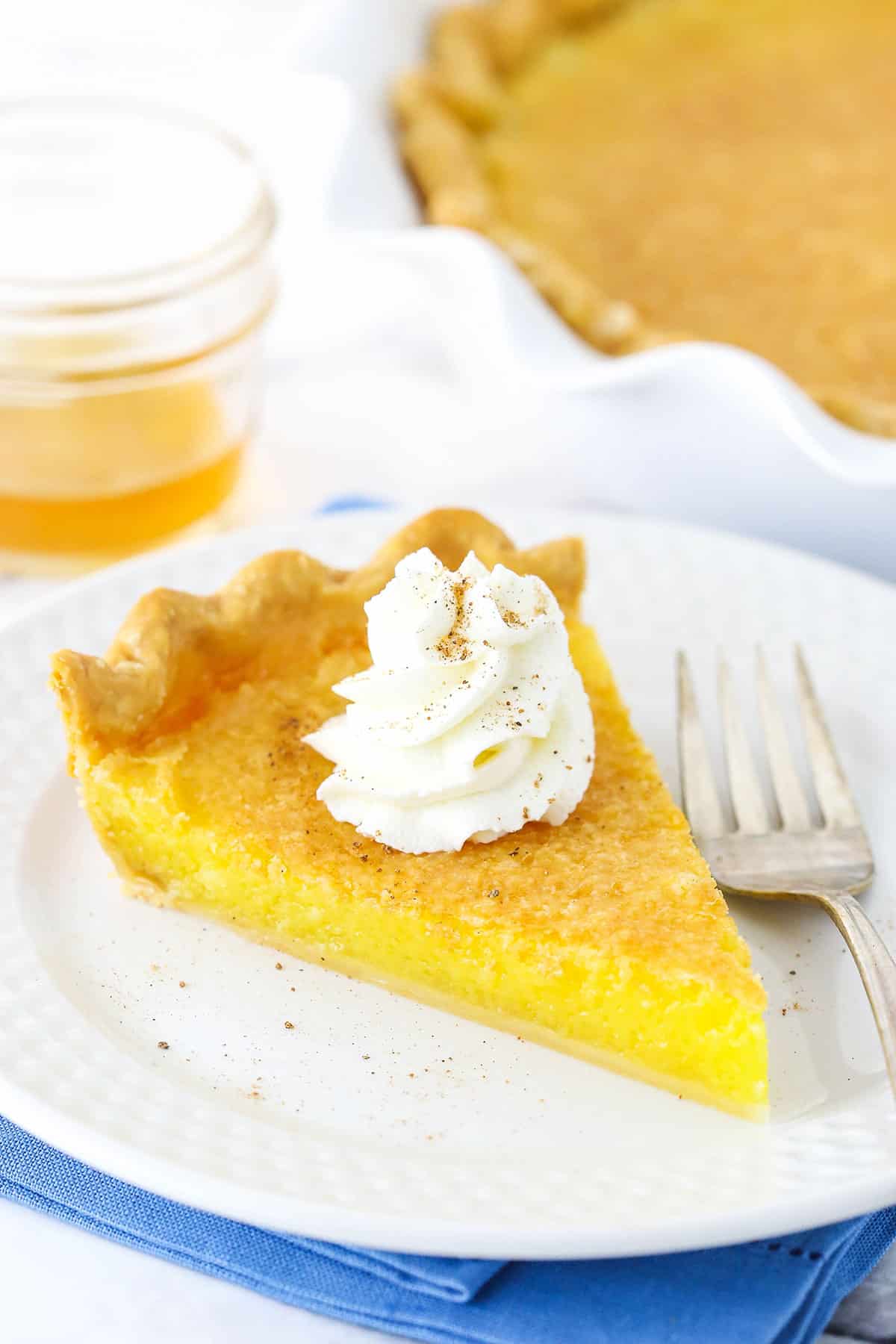 A slice of Vinegar Pie with a whipped cream swirl on a white plate next to a fork