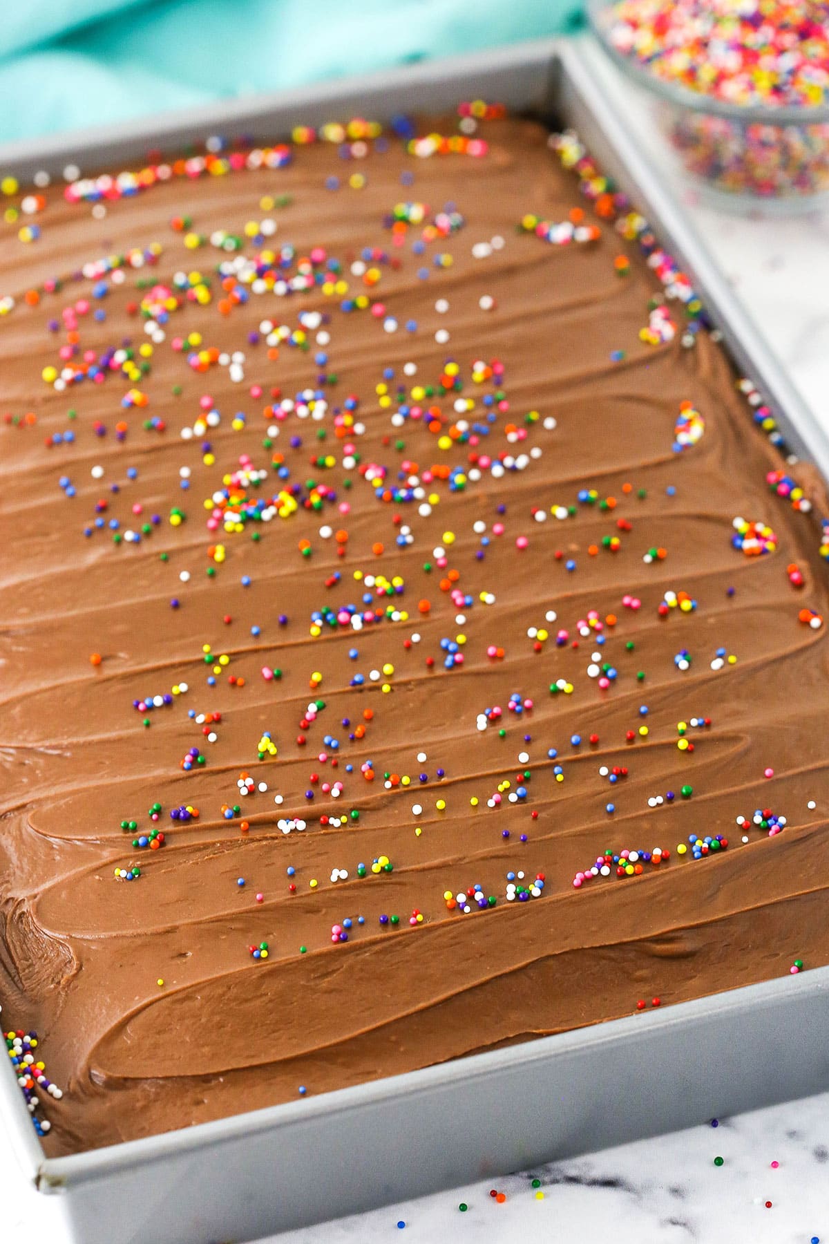 Overhead view of a full Wacky Cake with chocolate frosting and colorful sprinkles in a silver cake pan