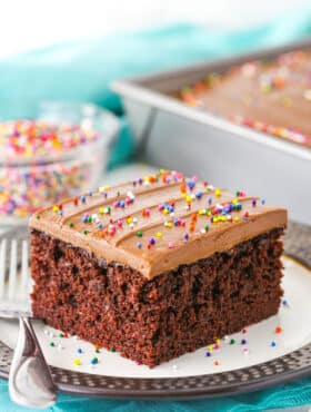 A single square serving of Wacky Cake with chocolate frosting and sprinkles on a white plate with a fork