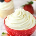 Whipped cream frosting in a decorative bowl near frosted cupcake surrounded by fresh berries.