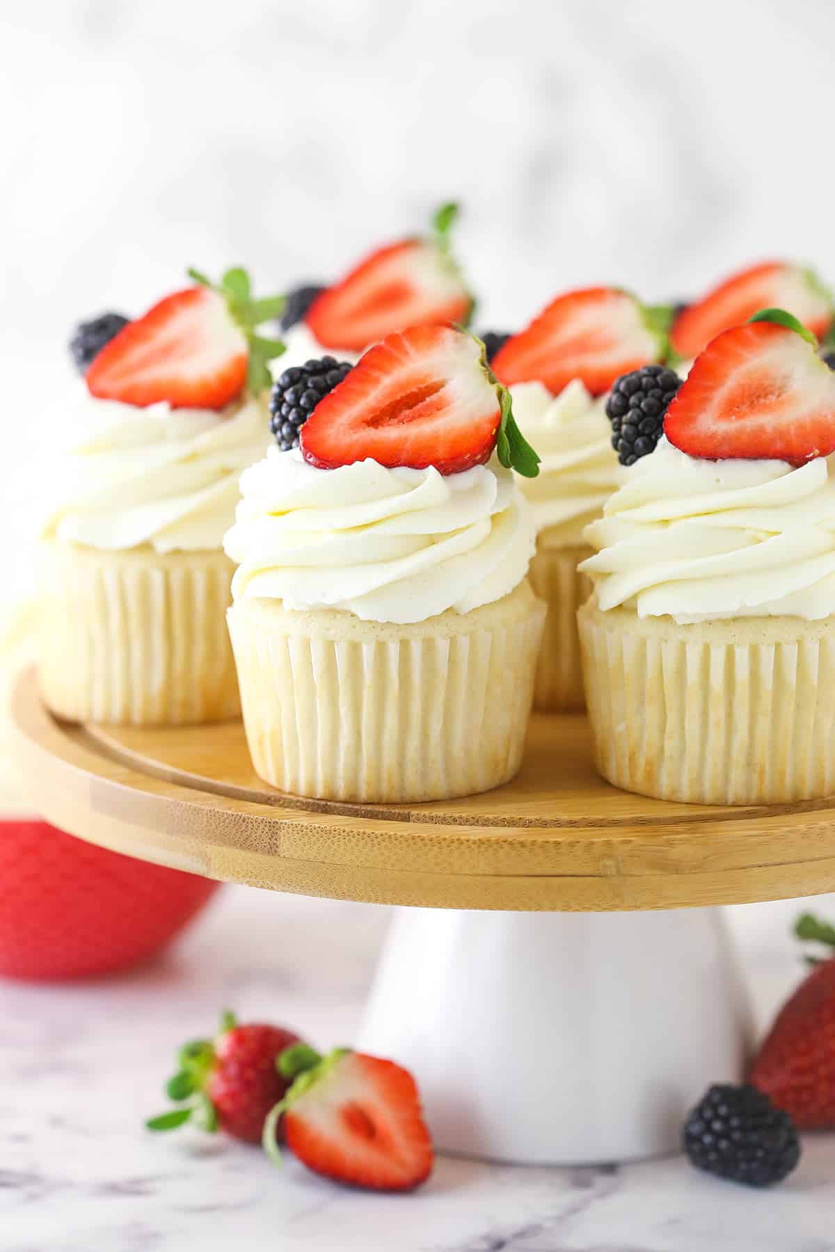 Cupcakes topped with whipped cream frosting and fresh berries on a cake stand surrounded by fresh berries