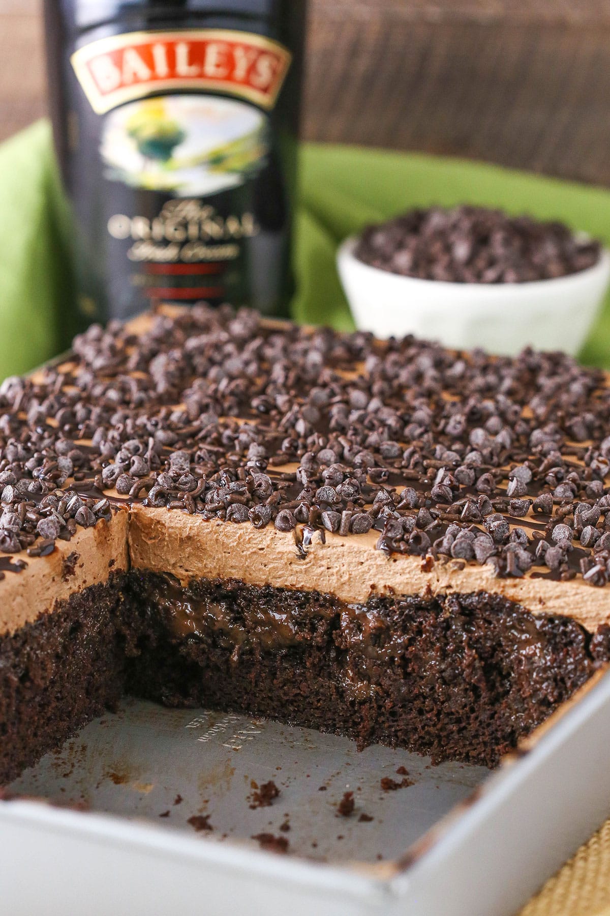 Baileys Chocolate Poke Cake topped with chocolate chips and a bottle of Baileys in the background