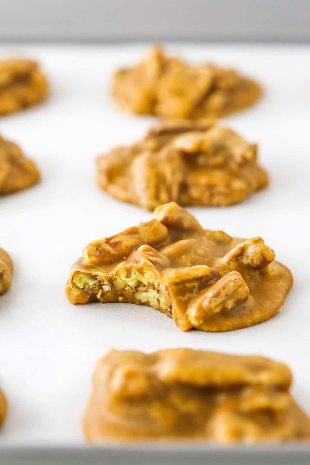 These are seriously the BEST Southern Praline Pecans! With the amazing flavor of brown sugar and butter, these are pure heaven! A little bit candy and a little bit cookie, they melt right in your mouth! Southern Pecan Pralines spread evenly and baked on a cookie sheet with one Southern Pecan Praline missing a bite