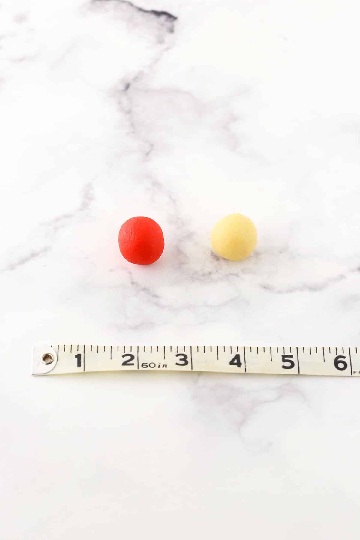 A step in making Red and white Candy Cane Cookies showing the portion of batter needed to roll in order to twist and shape the candy cane next to a tape measure