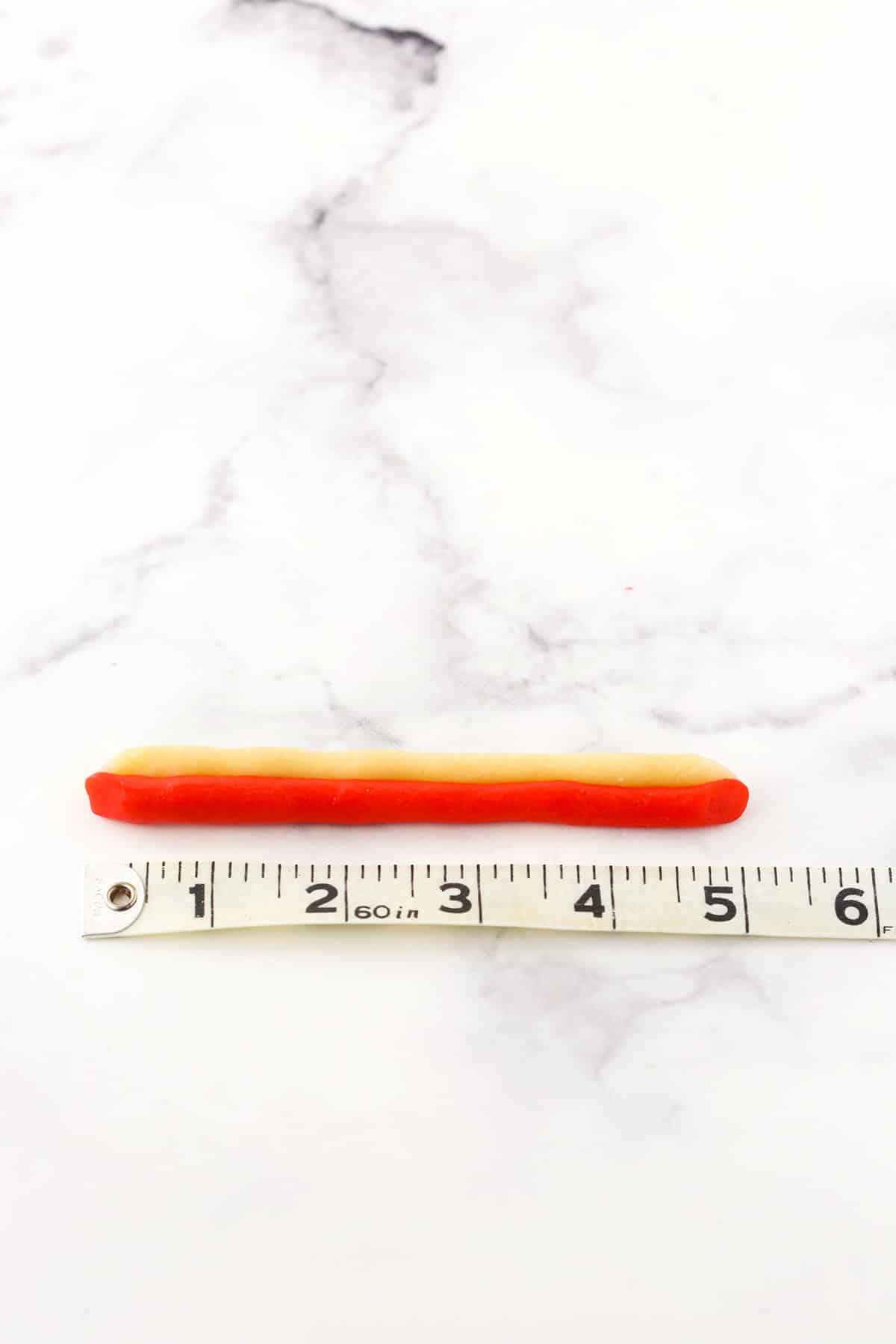 A step in making Red and white Candy Cane Cookies showing the twisting red and white batter to shape the candy cane next to a tape measure showing the scale and size