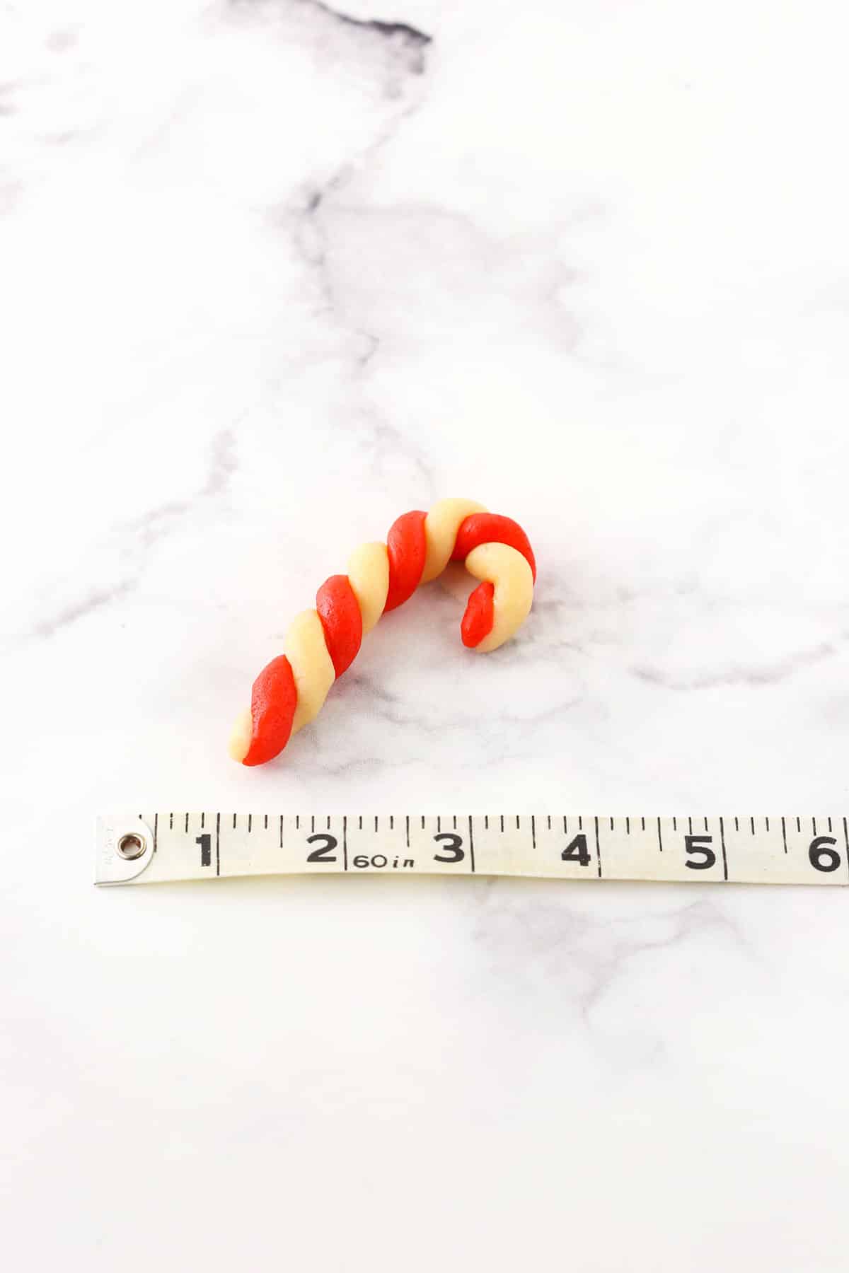 Red and white Candy Cane Cookie next to a tape measure showing the scale and size