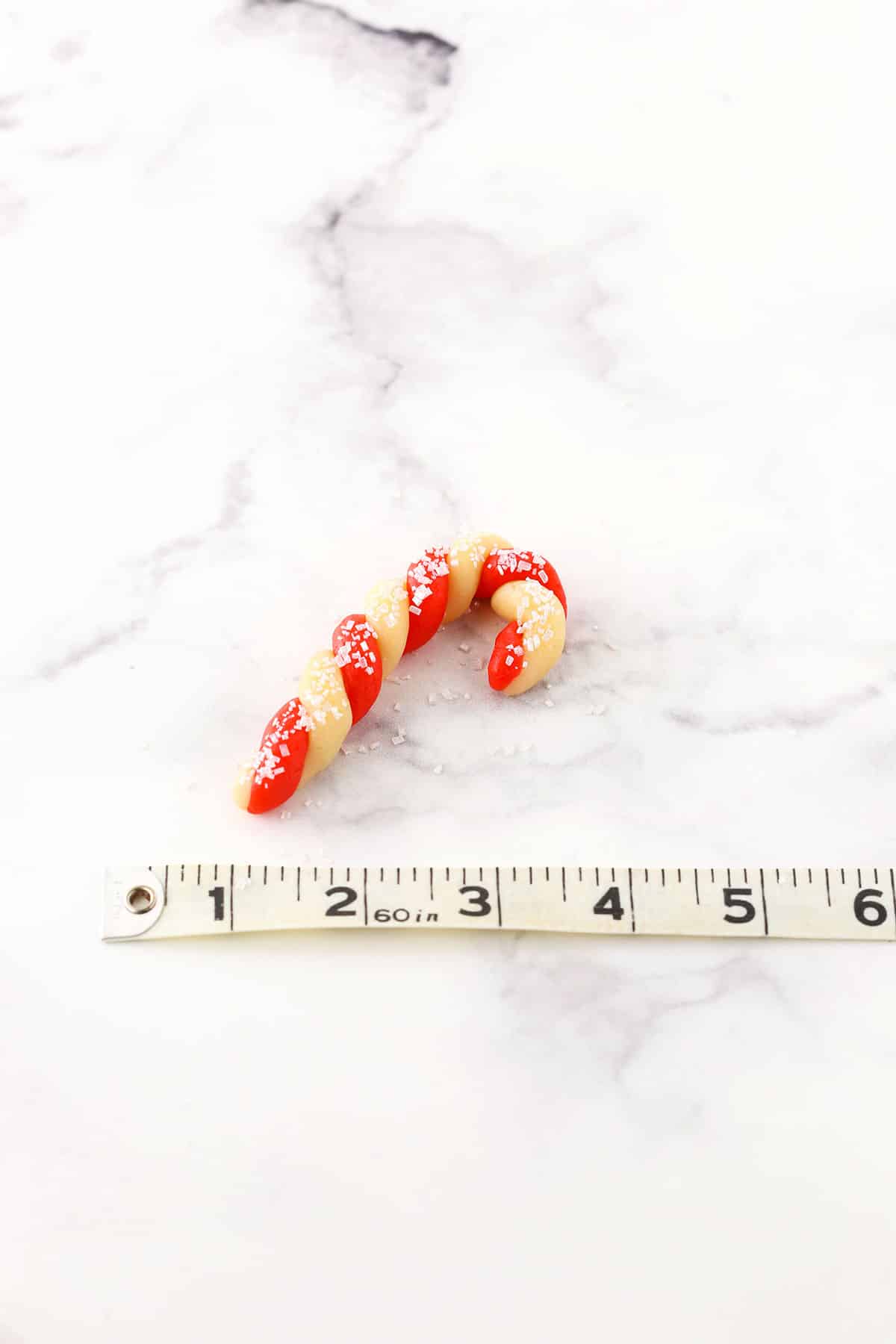 Red and white Candy Cane Cookie next to a tape measure showing the scale and size